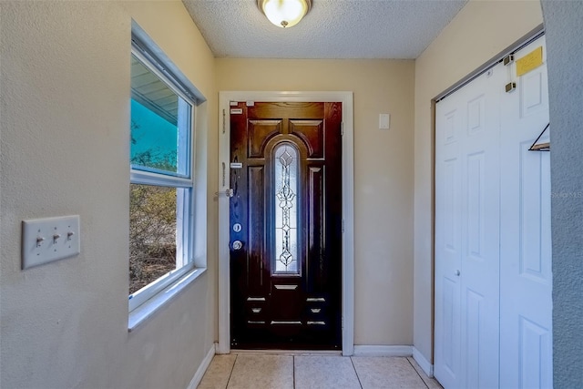 entryway with light tile patterned floors, a textured ceiling, and baseboards