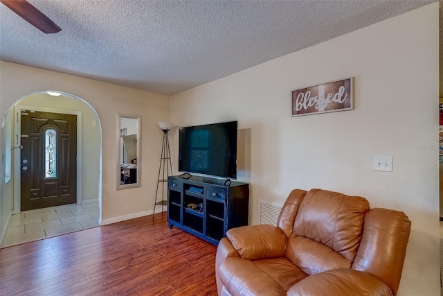 living area with visible vents, baseboards, wood finished floors, arched walkways, and a textured ceiling