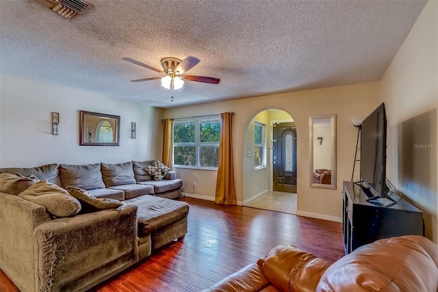 living room with baseboards, arched walkways, ceiling fan, wood-type flooring, and a textured ceiling