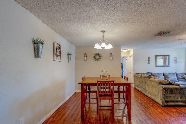 dining room with wood finished floors, visible vents, baseboards, an inviting chandelier, and a textured ceiling