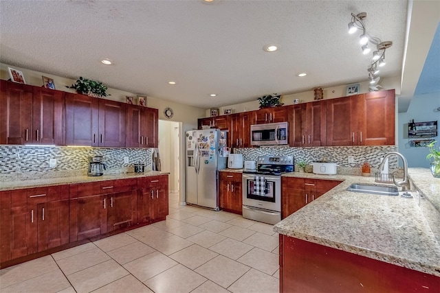 kitchen featuring a sink, light stone countertops, appliances with stainless steel finishes, light tile patterned flooring, and reddish brown cabinets