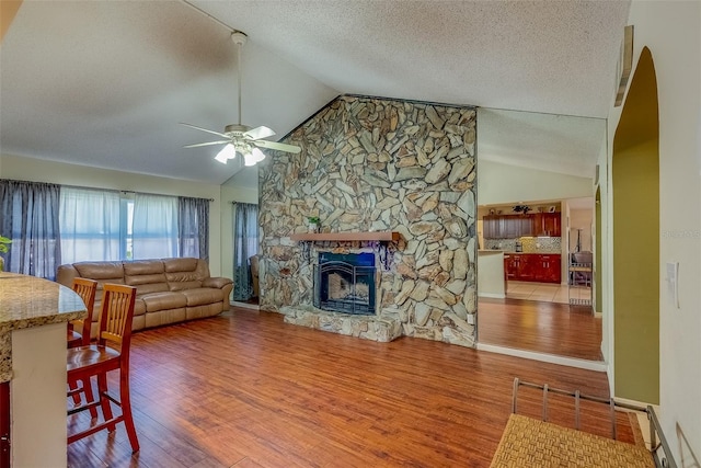 living room with a stone fireplace, a textured ceiling, wood finished floors, and ceiling fan