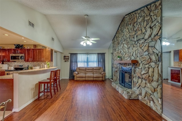 living room with visible vents, a textured ceiling, wood finished floors, a fireplace, and ceiling fan