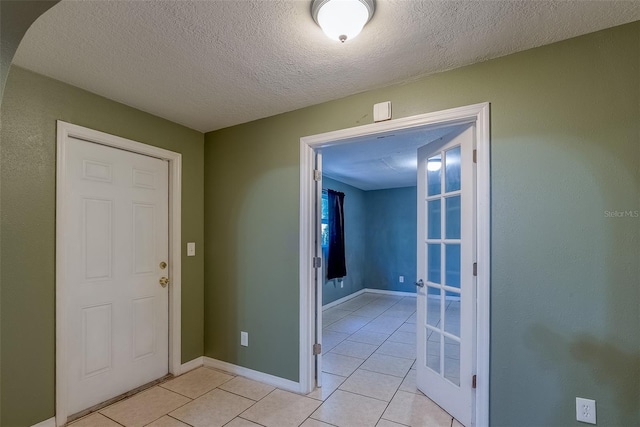 hallway featuring french doors, baseboards, a textured ceiling, and light tile patterned flooring