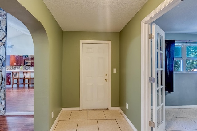 interior space with tile patterned floors, baseboards, arched walkways, and a textured ceiling