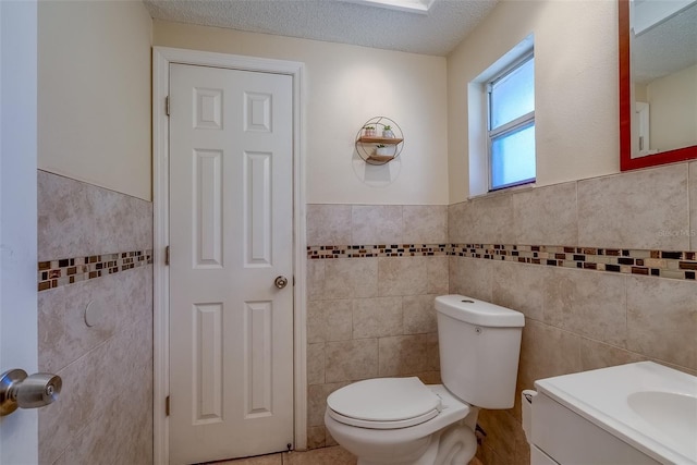 half bath featuring vanity, a wainscoted wall, a textured ceiling, tile walls, and toilet