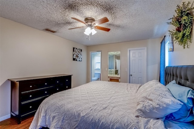 bedroom featuring wood finished floors, visible vents, ceiling fan, ensuite bathroom, and a textured ceiling