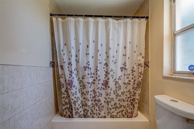 bathroom featuring shower / bathtub combination with curtain, toilet, tile walls, and a textured ceiling