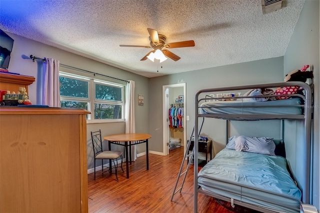 bedroom featuring a ceiling fan, baseboards, wood finished floors, visible vents, and a textured ceiling