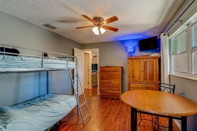 bedroom with visible vents, a textured ceiling, wood finished floors, and a ceiling fan