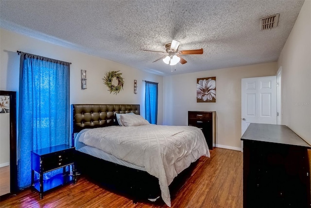 bedroom featuring ceiling fan, wood finished floors, visible vents, and a textured ceiling