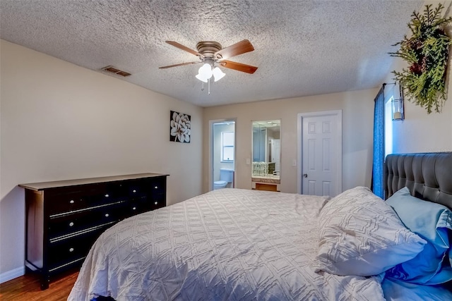 bedroom with wood finished floors, visible vents, ceiling fan, a textured ceiling, and connected bathroom