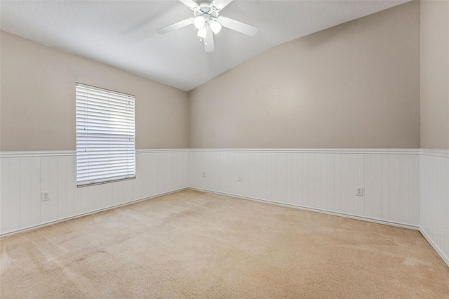 empty room featuring a wainscoted wall, carpet floors, a ceiling fan, and vaulted ceiling