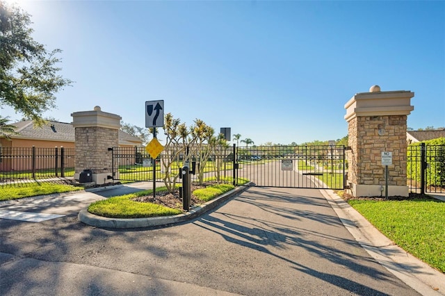 view of road featuring a gated entry, curbs, traffic signs, and a gate