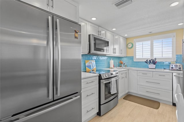 kitchen featuring visible vents, light countertops, appliances with stainless steel finishes, white cabinetry, and backsplash