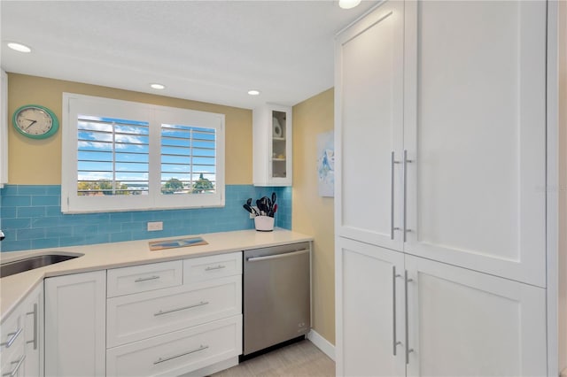 kitchen featuring a sink, backsplash, white cabinetry, light countertops, and dishwasher