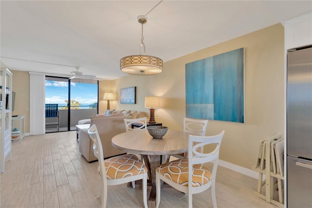 dining area with light wood finished floors, ceiling fan, baseboards, and expansive windows