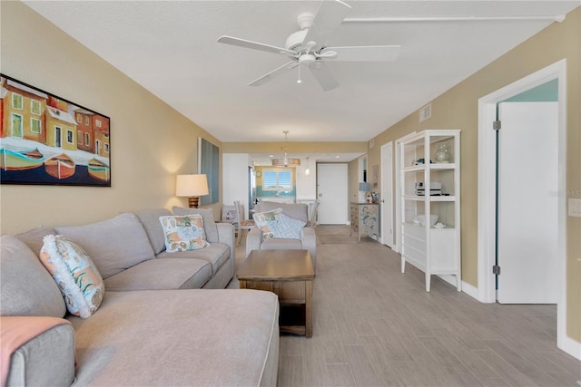 living area with light wood-type flooring, visible vents, and ceiling fan with notable chandelier