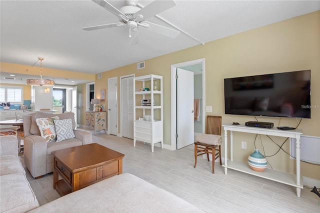 living room with baseboards, wood finished floors, visible vents, and ceiling fan