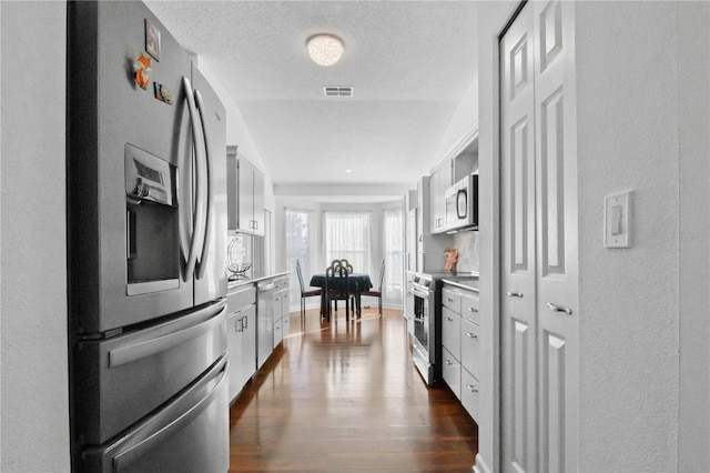 kitchen featuring visible vents, stainless steel appliances, dark wood-type flooring, light countertops, and white cabinetry