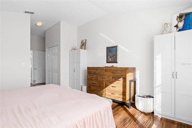 bedroom featuring a closet, visible vents, lofted ceiling, and wood finished floors