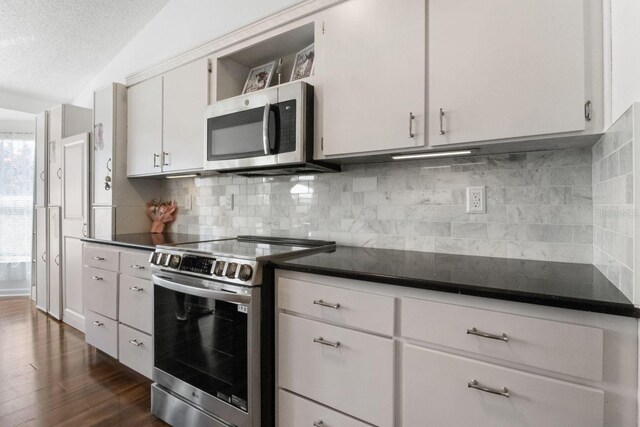 2325 W Del Webb Blvd, Sun City Center, FL 33573 - kitchen featuring a textured ceiling, stainless steel appliances, dark countertops, dark wood finished floors, and backsplash