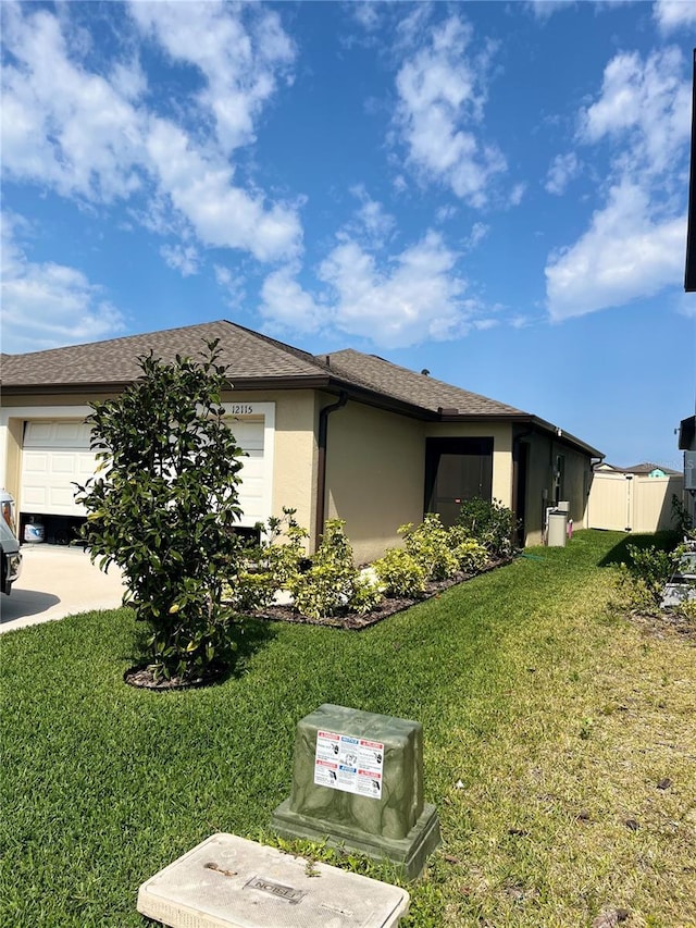 view of side of home featuring a lawn, fence, a garage, and stucco siding