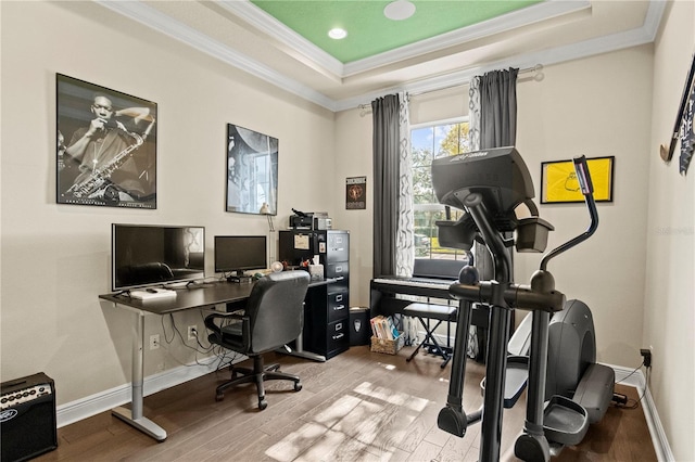 office space with a raised ceiling, wood finished floors, baseboards, and ornamental molding