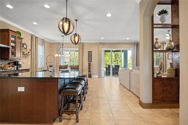 kitchen with dark countertops, glass insert cabinets, crown molding, a breakfast bar, and a sink