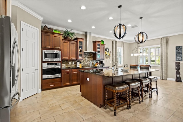 kitchen featuring a kitchen bar, an island with sink, backsplash, appliances with stainless steel finishes, and wall chimney range hood