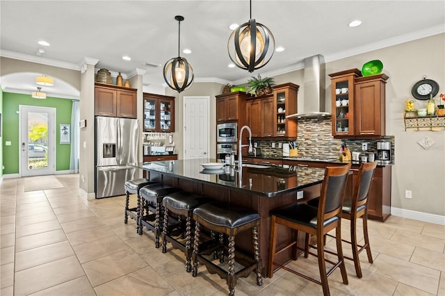 kitchen featuring appliances with stainless steel finishes, a kitchen breakfast bar, arched walkways, wall chimney exhaust hood, and a sink