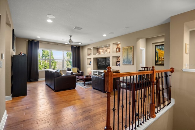 living area featuring built in features, baseboards, light wood-type flooring, and ceiling fan