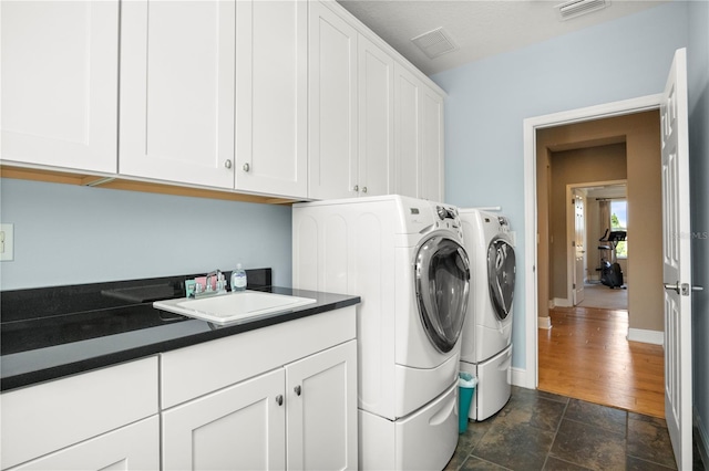 clothes washing area with a sink, visible vents, cabinet space, and washing machine and dryer