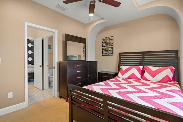 bedroom with arched walkways, visible vents, light colored carpet, and connected bathroom