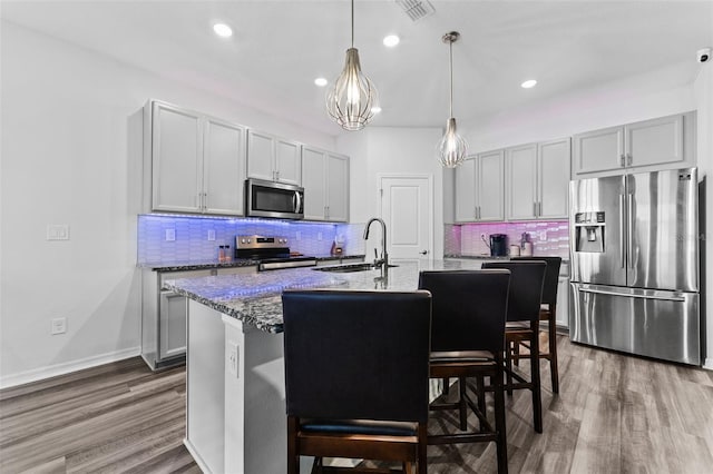 kitchen featuring a sink, dark wood finished floors, stone counters, appliances with stainless steel finishes, and a kitchen island with sink