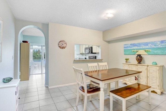 dining space featuring light tile patterned floors, baseboards, arched walkways, and a textured ceiling