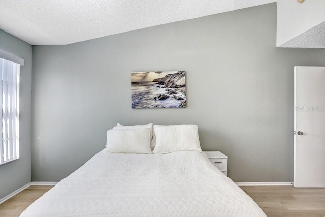 bedroom with light wood finished floors, a textured ceiling, and baseboards