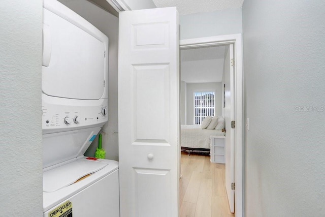 washroom with light wood-type flooring, stacked washer / drying machine, and laundry area