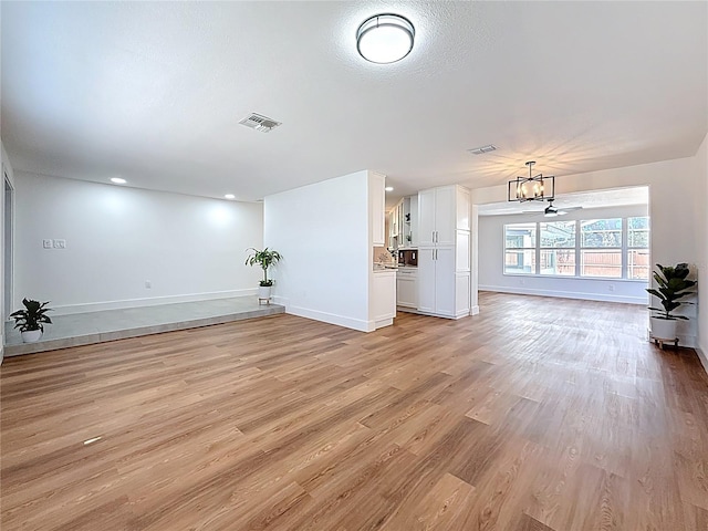 unfurnished living room featuring an inviting chandelier, baseboards, visible vents, and light wood finished floors