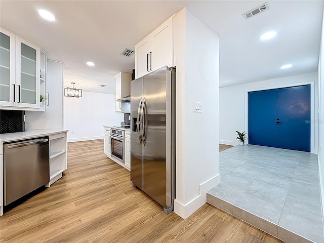 kitchen with visible vents, glass insert cabinets, light wood-type flooring, appliances with stainless steel finishes, and white cabinetry