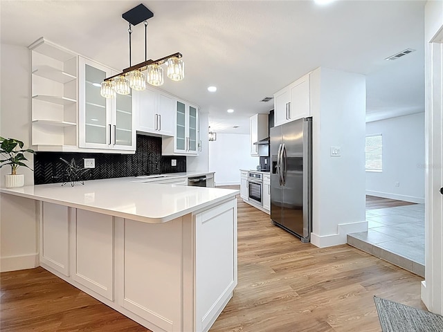 kitchen with light wood finished floors, visible vents, backsplash, a peninsula, and stainless steel appliances