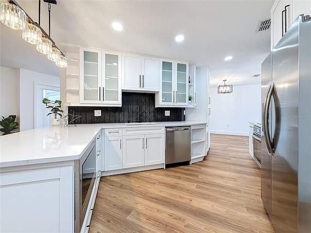 kitchen with open shelves, a sink, tasteful backsplash, appliances with stainless steel finishes, and light wood finished floors