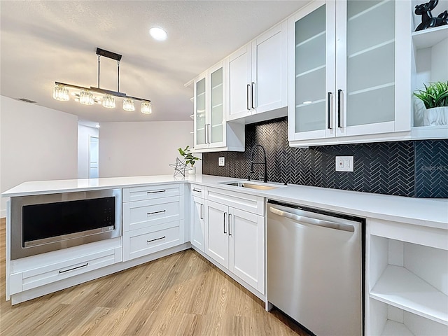 kitchen with light countertops, light wood-style flooring, appliances with stainless steel finishes, a peninsula, and a sink