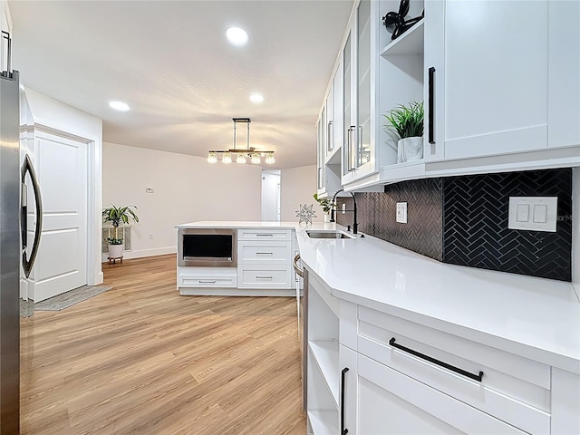 kitchen with open shelves, light wood-style flooring, freestanding refrigerator, a sink, and tasteful backsplash