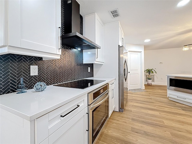 kitchen with visible vents, white cabinets, light wood-style floors, appliances with stainless steel finishes, and wall chimney range hood