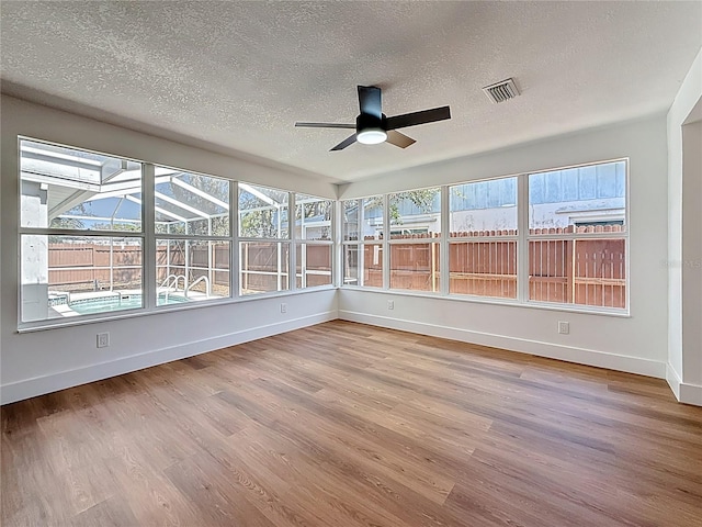 unfurnished sunroom with a wealth of natural light, visible vents, and ceiling fan