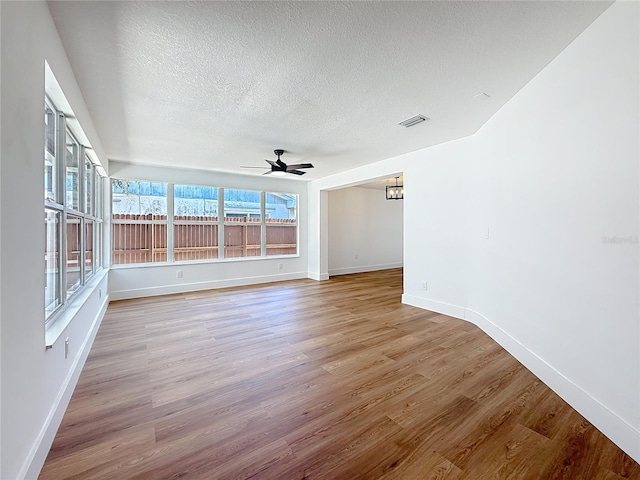 spare room featuring visible vents, a textured ceiling, light wood finished floors, baseboards, and ceiling fan