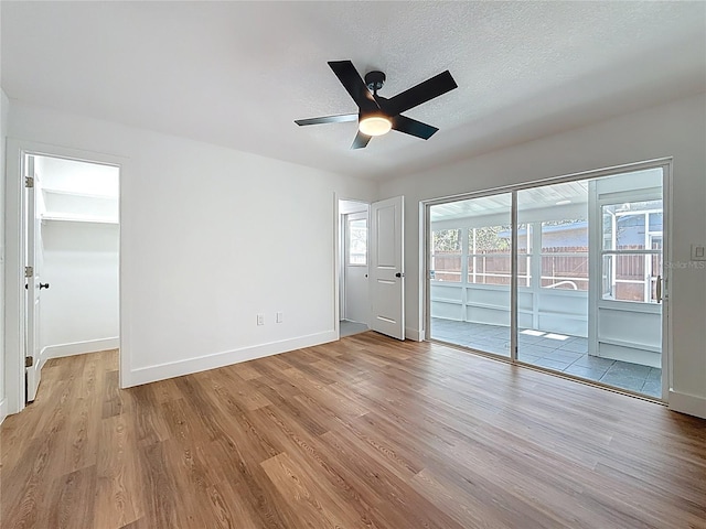 interior space featuring a textured ceiling, light wood-style flooring, baseboards, and ceiling fan