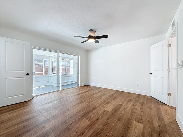 empty room with wood finished floors, baseboards, visible vents, ceiling fan, and a textured ceiling