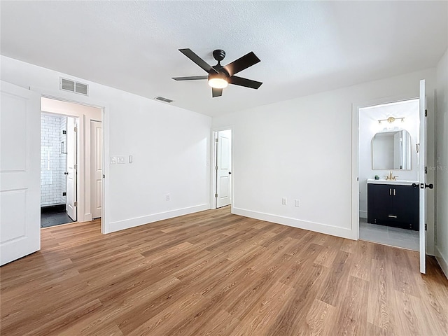 unfurnished bedroom featuring ensuite bath, light wood-style floors, and visible vents